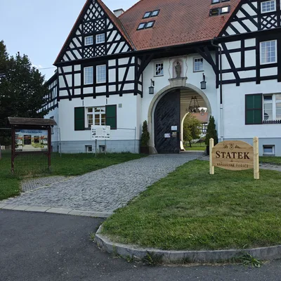 Brána Statku v Královském Poříčí s dřevěnou cedulí u příjezdové cesty
